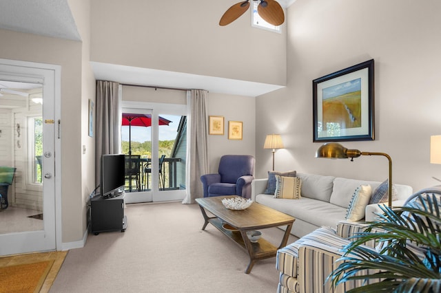 living area featuring ceiling fan, a towering ceiling, a wealth of natural light, and light carpet