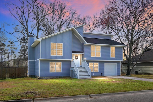 bi-level home featuring a chimney, an attached garage, a front yard, fence, and driveway