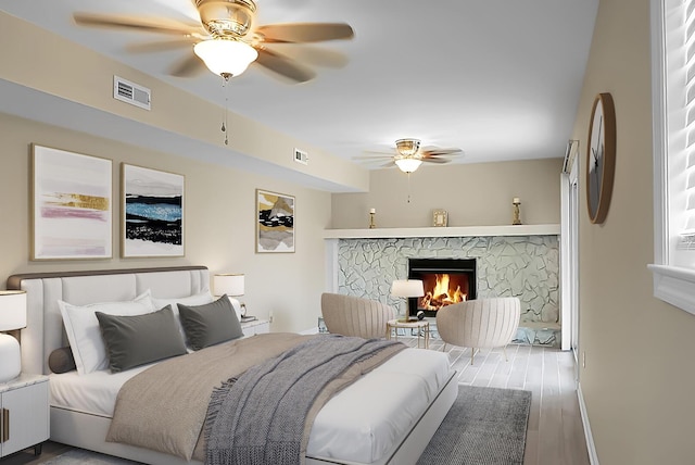 bedroom with a stone fireplace, wood finished floors, visible vents, and a ceiling fan