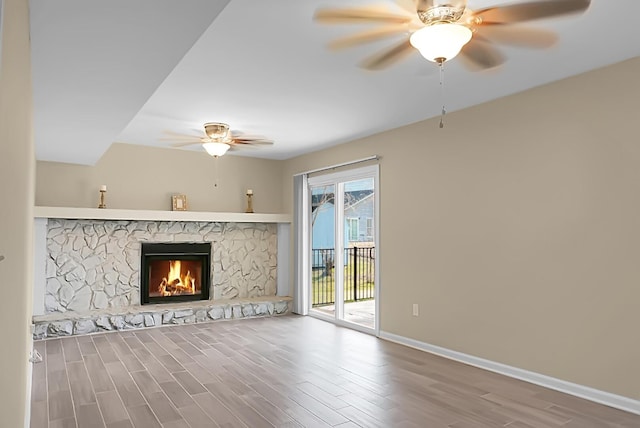 unfurnished living room featuring a stone fireplace, wood finished floors, a ceiling fan, and baseboards