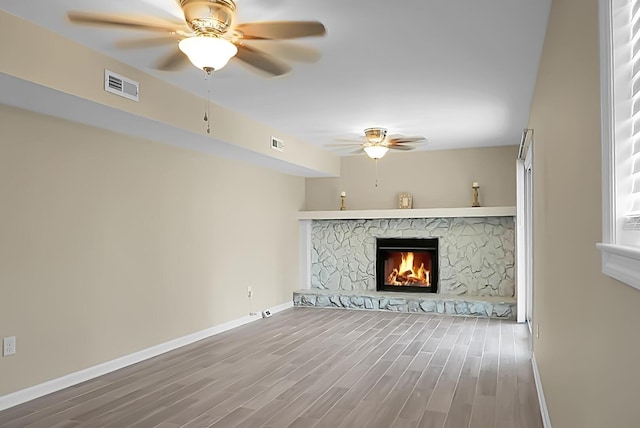 unfurnished living room with a stone fireplace, wood finished floors, visible vents, and baseboards