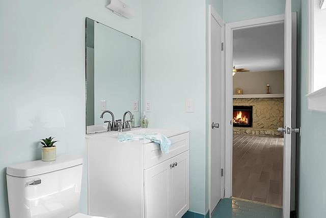 bathroom featuring a ceiling fan, a fireplace, vanity, and toilet