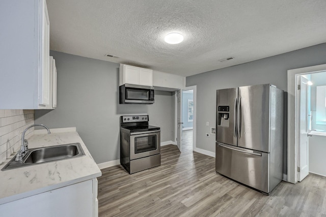 kitchen with visible vents, appliances with stainless steel finishes, light wood-type flooring, white cabinetry, and a sink