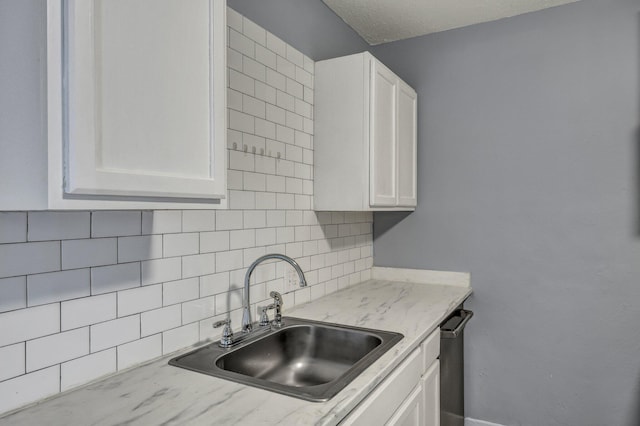 kitchen with backsplash, white cabinets, and a sink