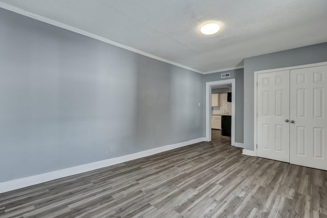 unfurnished bedroom featuring a textured ceiling, wood finished floors, baseboards, a closet, and crown molding