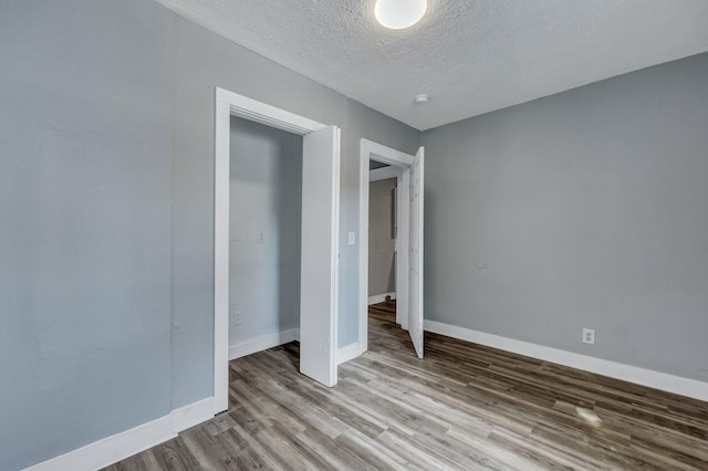 unfurnished bedroom with a textured ceiling, baseboards, and wood finished floors