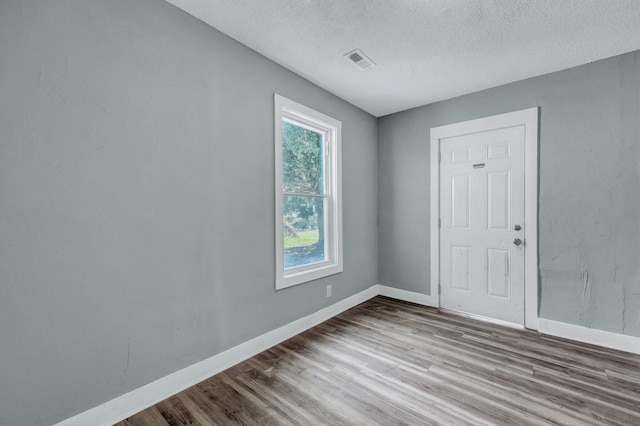 spare room featuring a textured ceiling, wood finished floors, visible vents, and baseboards