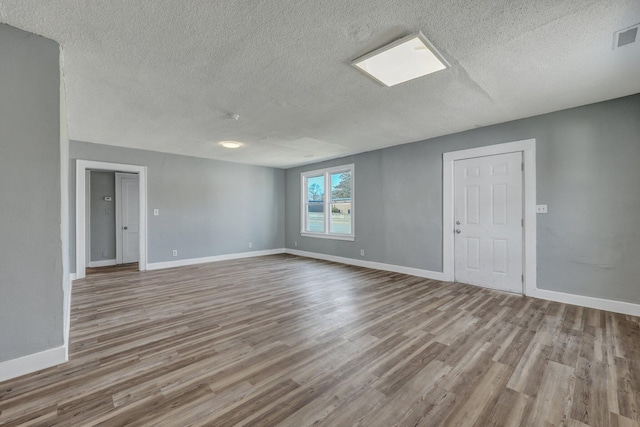 empty room with a textured ceiling, wood finished floors, and baseboards