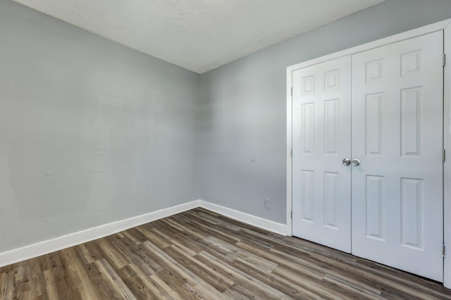 unfurnished bedroom with dark wood-style floors, a closet, a textured ceiling, and baseboards