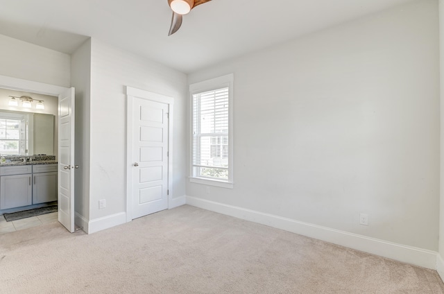 unfurnished bedroom with a closet, connected bathroom, light carpet, and ceiling fan