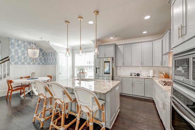 kitchen featuring a kitchen island with sink, decorative light fixtures, dark wood-type flooring, stainless steel appliances, and sink