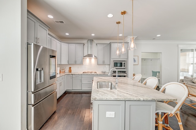 kitchen featuring dark hardwood / wood-style flooring, appliances with stainless steel finishes, wall chimney range hood, a kitchen bar, and sink