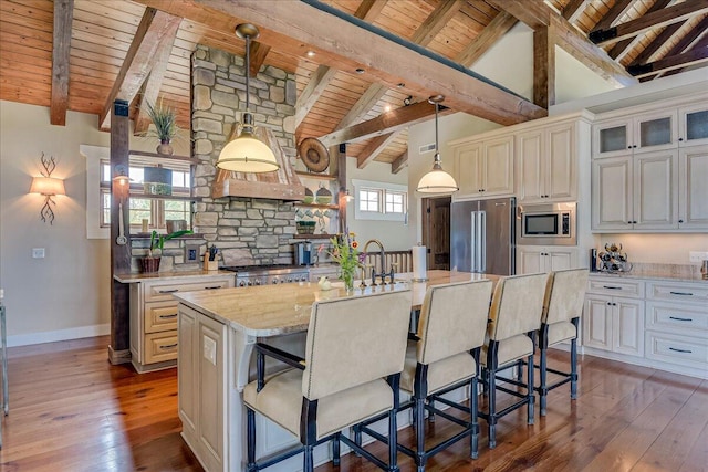 kitchen featuring appliances with stainless steel finishes, a breakfast bar, an island with sink, light stone counters, and pendant lighting