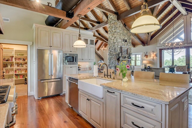 kitchen with pendant lighting, beam ceiling, sink, built in appliances, and a center island with sink