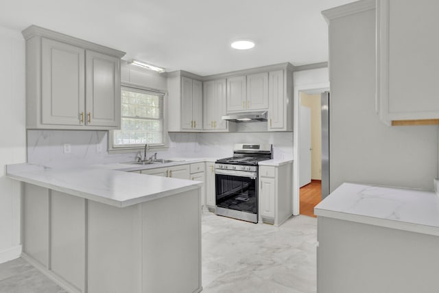 kitchen with decorative backsplash, kitchen peninsula, sink, and stainless steel range with gas stovetop