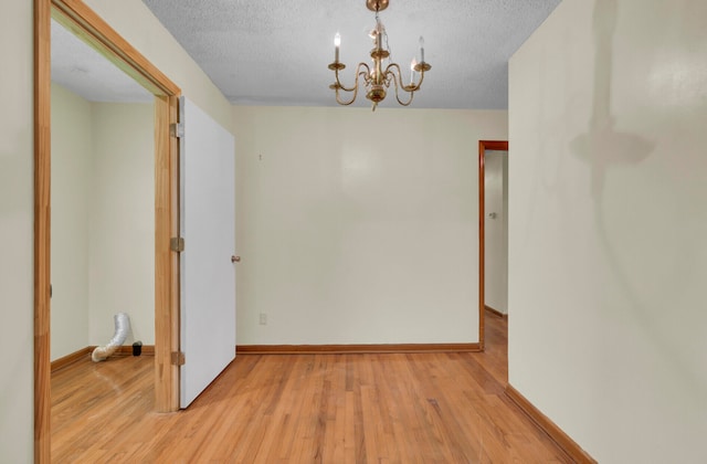 spare room featuring an inviting chandelier, a textured ceiling, and light hardwood / wood-style flooring