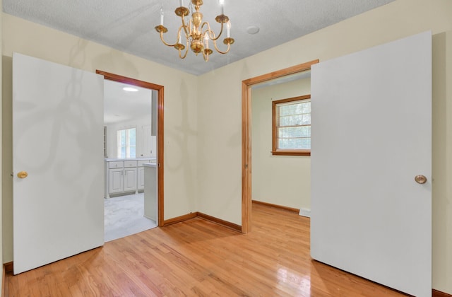 empty room featuring light wood-type flooring, a chandelier, and plenty of natural light