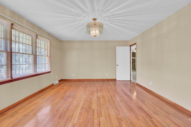 unfurnished room with a textured ceiling, light hardwood / wood-style floors, and a chandelier