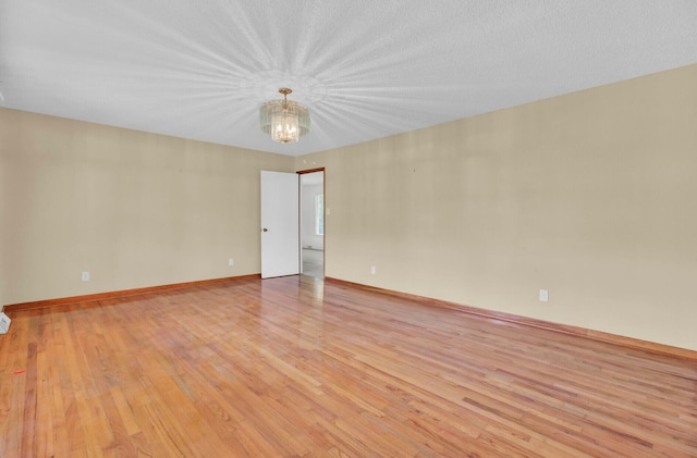 unfurnished room with a textured ceiling, light hardwood / wood-style flooring, and a notable chandelier