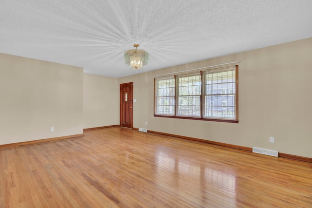 unfurnished room featuring a notable chandelier, a textured ceiling, and light hardwood / wood-style flooring