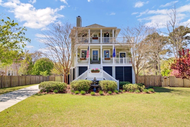 beach home featuring a front yard, covered porch, stairway, fence, and a balcony