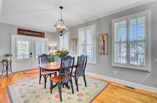 dining area featuring a notable chandelier, crown molding, wood finished floors, baseboards, and visible vents