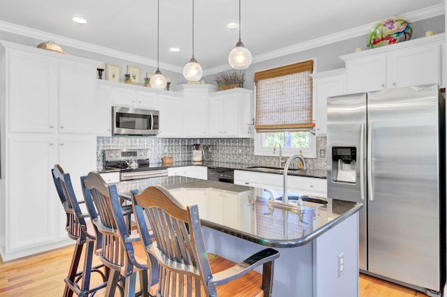 kitchen with crown molding, appliances with stainless steel finishes, a center island with sink, light wood-type flooring, and white cabinets