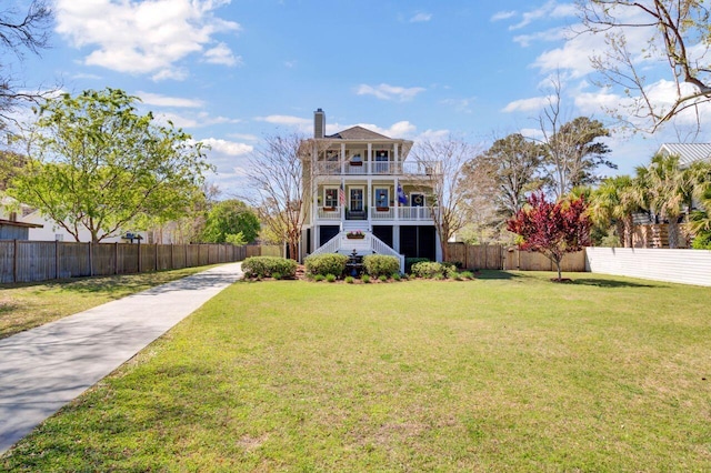 rear view of property featuring stairs, a balcony, fence private yard, a yard, and a chimney
