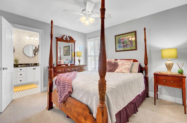 bedroom with light colored carpet, ceiling fan, baseboards, and ensuite bath