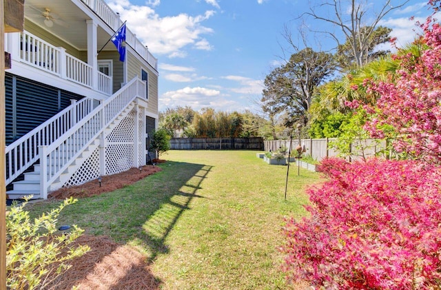 view of yard with a ceiling fan, fence, and stairs
