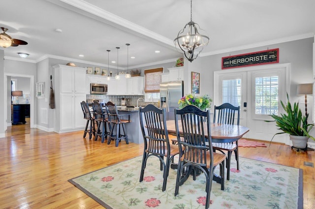 dining room featuring crown molding, ceiling fan with notable chandelier, light wood-type flooring, baseboards, and visible vents