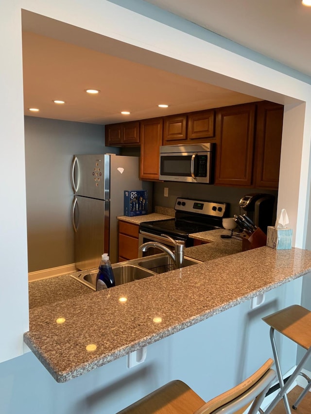 kitchen with a breakfast bar, kitchen peninsula, appliances with stainless steel finishes, and stone countertops