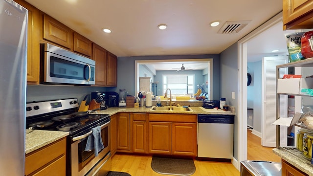 kitchen featuring light hardwood / wood-style floors, stainless steel appliances, sink, ceiling fan, and light stone counters