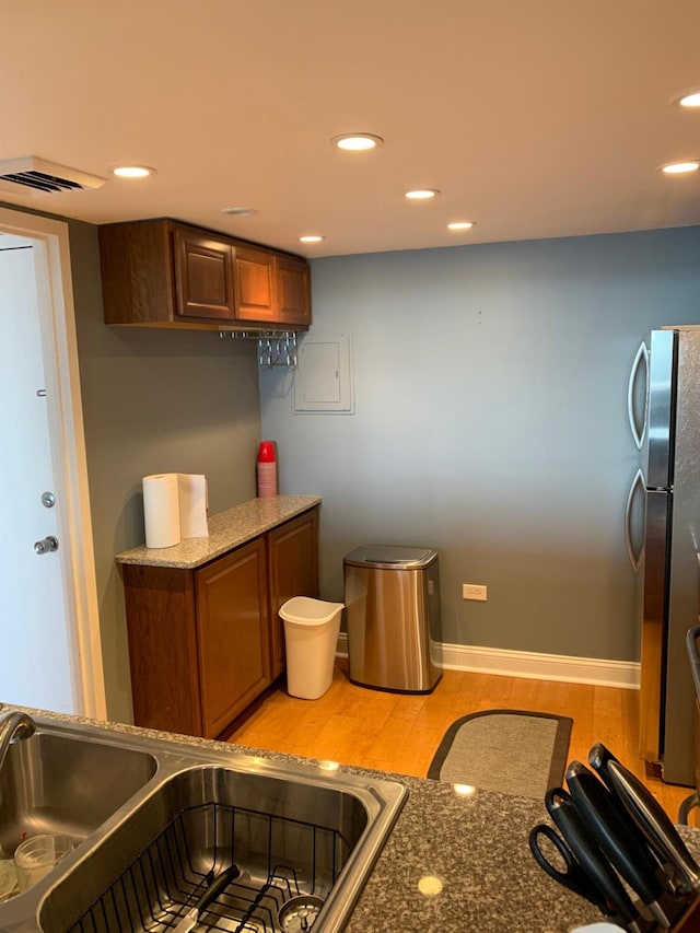 kitchen with light hardwood / wood-style flooring, stainless steel refrigerator, sink, and stone counters