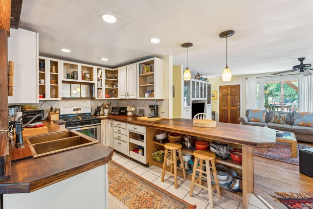 kitchen featuring light tile patterned floors, sink, ceiling fan, stainless steel range with gas cooktop, and tasteful backsplash