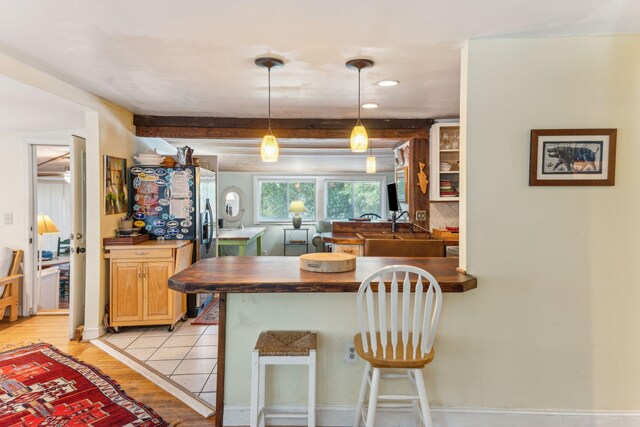 kitchen featuring light hardwood / wood-style flooring, sink, kitchen peninsula, beam ceiling, and a breakfast bar