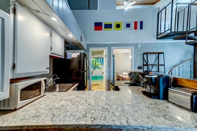 kitchen featuring sink, wooden walls, black appliances, and ceiling fan