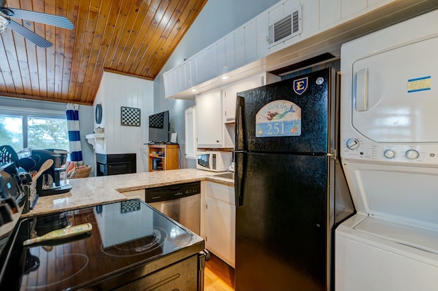 kitchen featuring stacked washing maching and dryer, black refrigerator, lofted ceiling, white cabinets, and stainless steel dishwasher