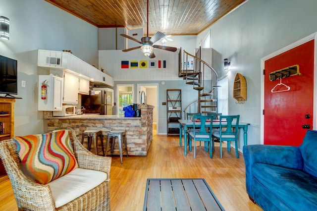 living room featuring a high ceiling, ornamental molding, ceiling fan, wood ceiling, and light hardwood / wood-style floors