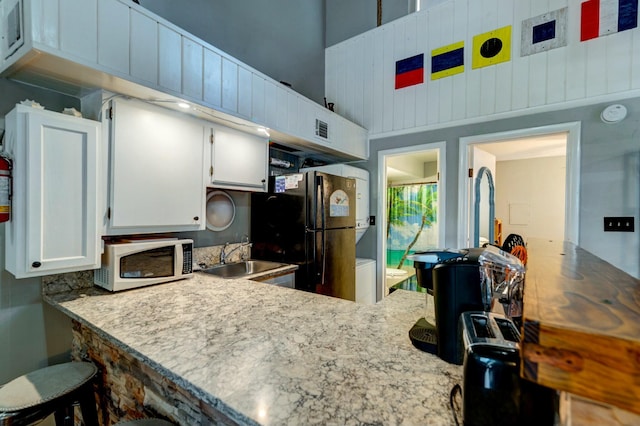 kitchen with black fridge, sink, white cabinets, and kitchen peninsula