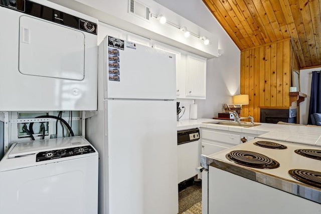 kitchen featuring white appliances, vaulted ceiling, sink, stacked washer and dryer, and white cabinetry