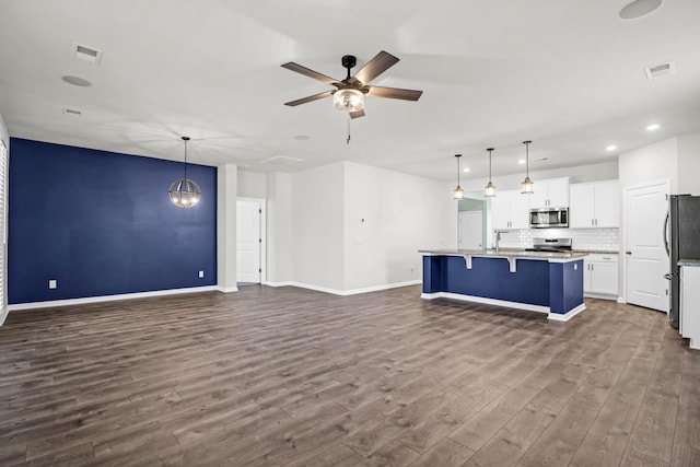 kitchen with decorative light fixtures, a center island with sink, stainless steel appliances, open floor plan, and white cabinets