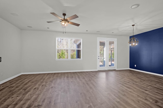 spare room with ceiling fan with notable chandelier, wood finished floors, visible vents, and baseboards