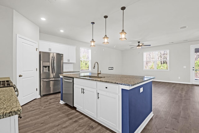 kitchen featuring a sink, white cabinets, appliances with stainless steel finishes, dark stone counters, and a center island with sink