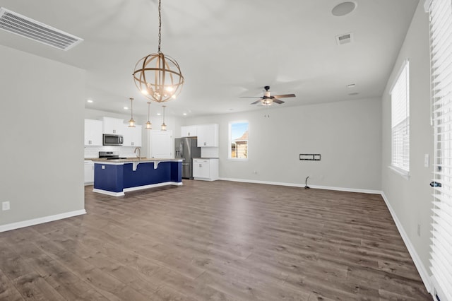 unfurnished living room featuring baseboards, visible vents, wood finished floors, ceiling fan with notable chandelier, and recessed lighting