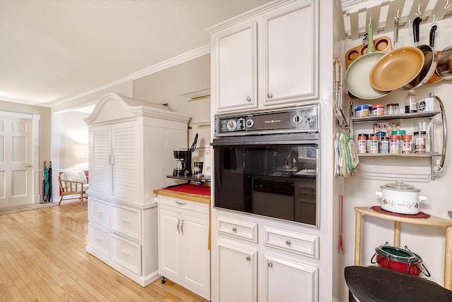 kitchen with crown molding, light hardwood / wood-style floors, and black oven