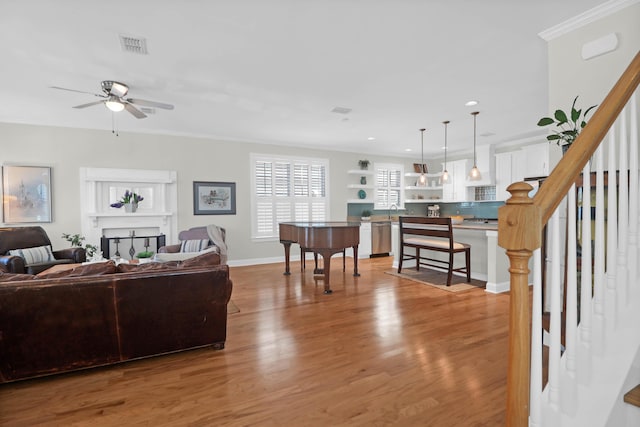 living room with a ceiling fan, baseboards, stairs, light wood finished floors, and crown molding