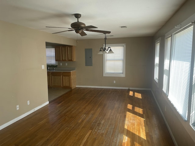 unfurnished living room with dark wood-style flooring, electric panel, baseboards, and ceiling fan with notable chandelier