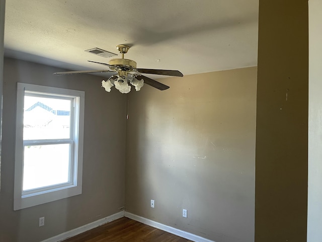 spare room with dark wood-style floors, visible vents, baseboards, and a ceiling fan