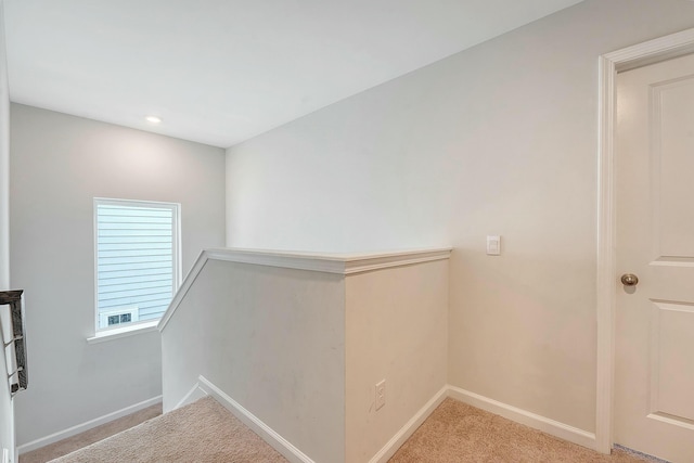 hallway featuring light carpet, baseboards, and an upstairs landing